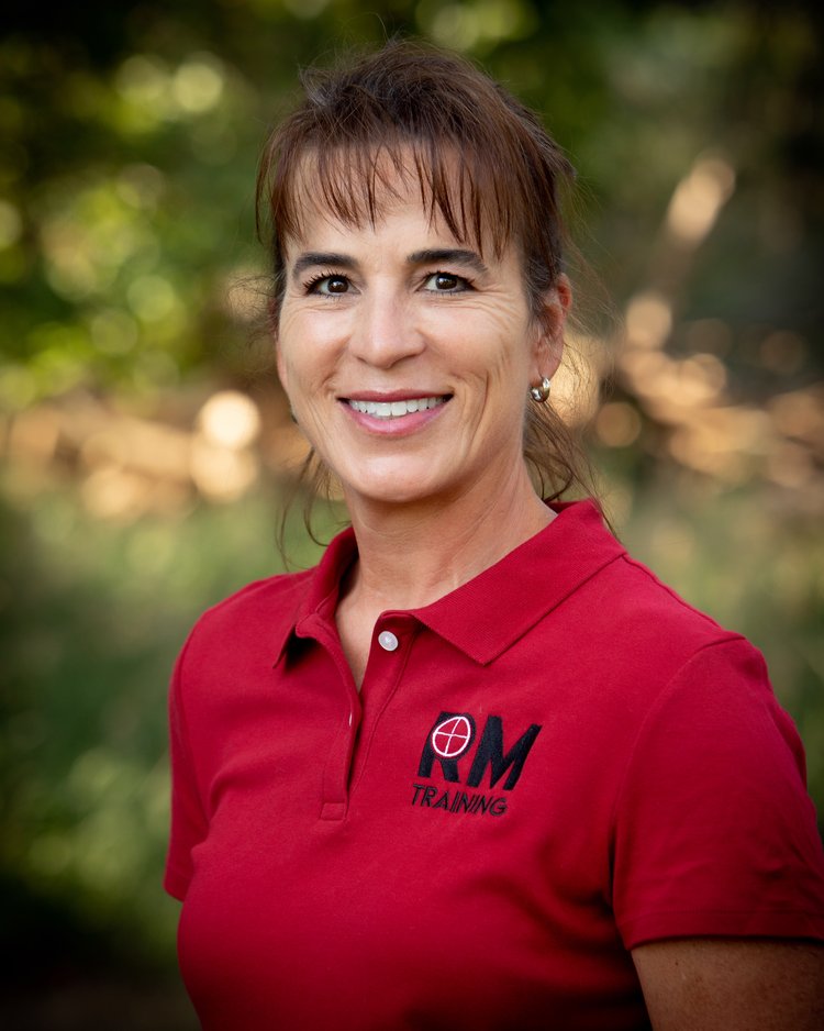 Instructor Cate is a thin woman with brown hair and a large professional smile. Cate is wearing  a red RAM Master Training polo shirt.