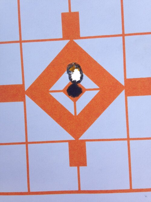 A Paper one inch grid target in orange with a white background displaying three bullet holes in close proximity.
